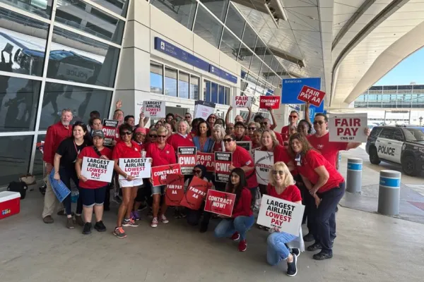 American Airlines passenger service workers in red shirts holding signs that read "Largest Airline Lowest Pay"