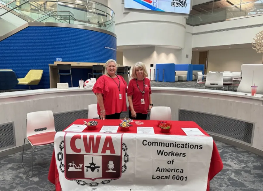Two CWA members in red shirts stand behind a table with a CWA Local 6001 sign
